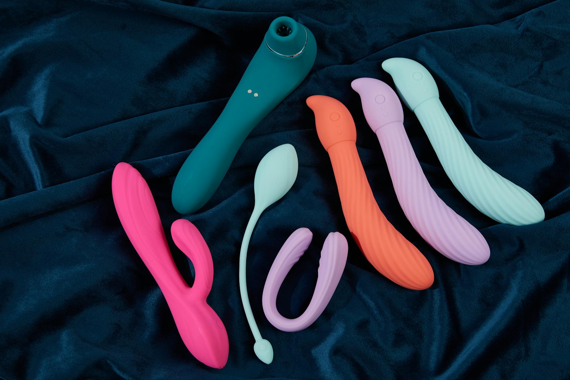 Collection of colorful silicone sex toys arranged on dark fabric, illustrating different vibrator styles and shapes.