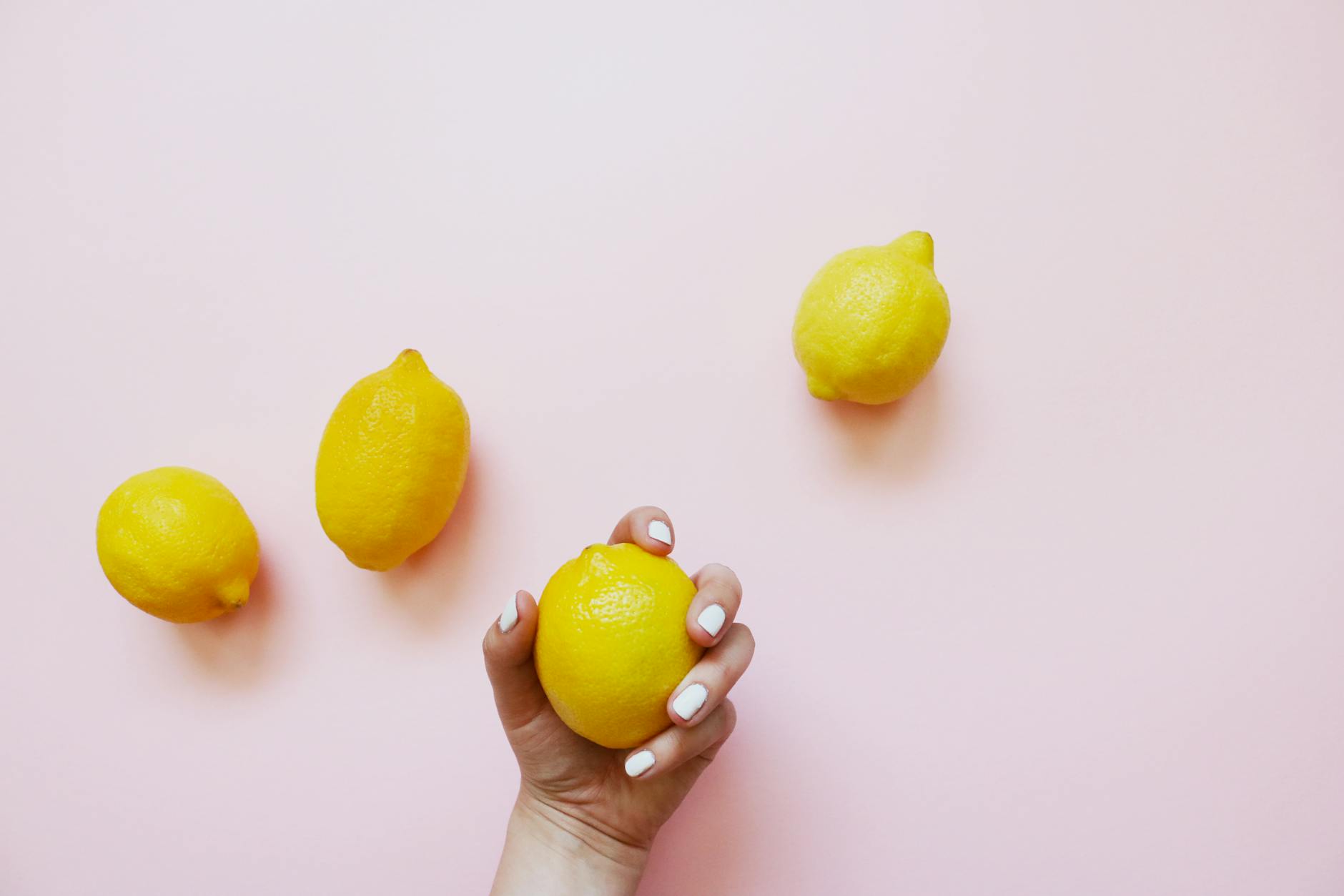 Hand holding a fresh lemon on soft pink background with additional lemons, representing sensory pleasure and wellness