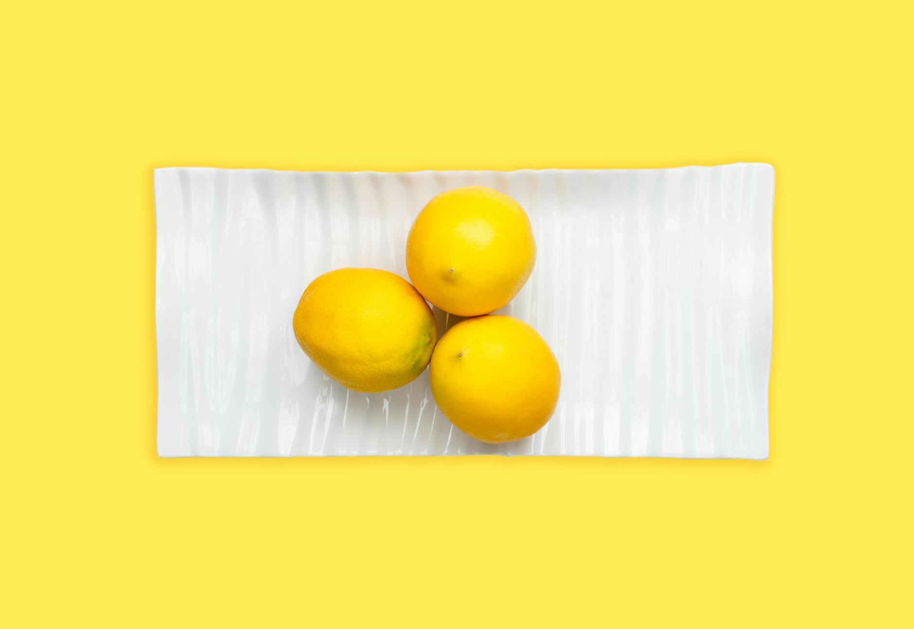 Fresh lemons arranged on white plate with yellow background, symbolizing the bright, effective pleasure of lemon vibrator technology