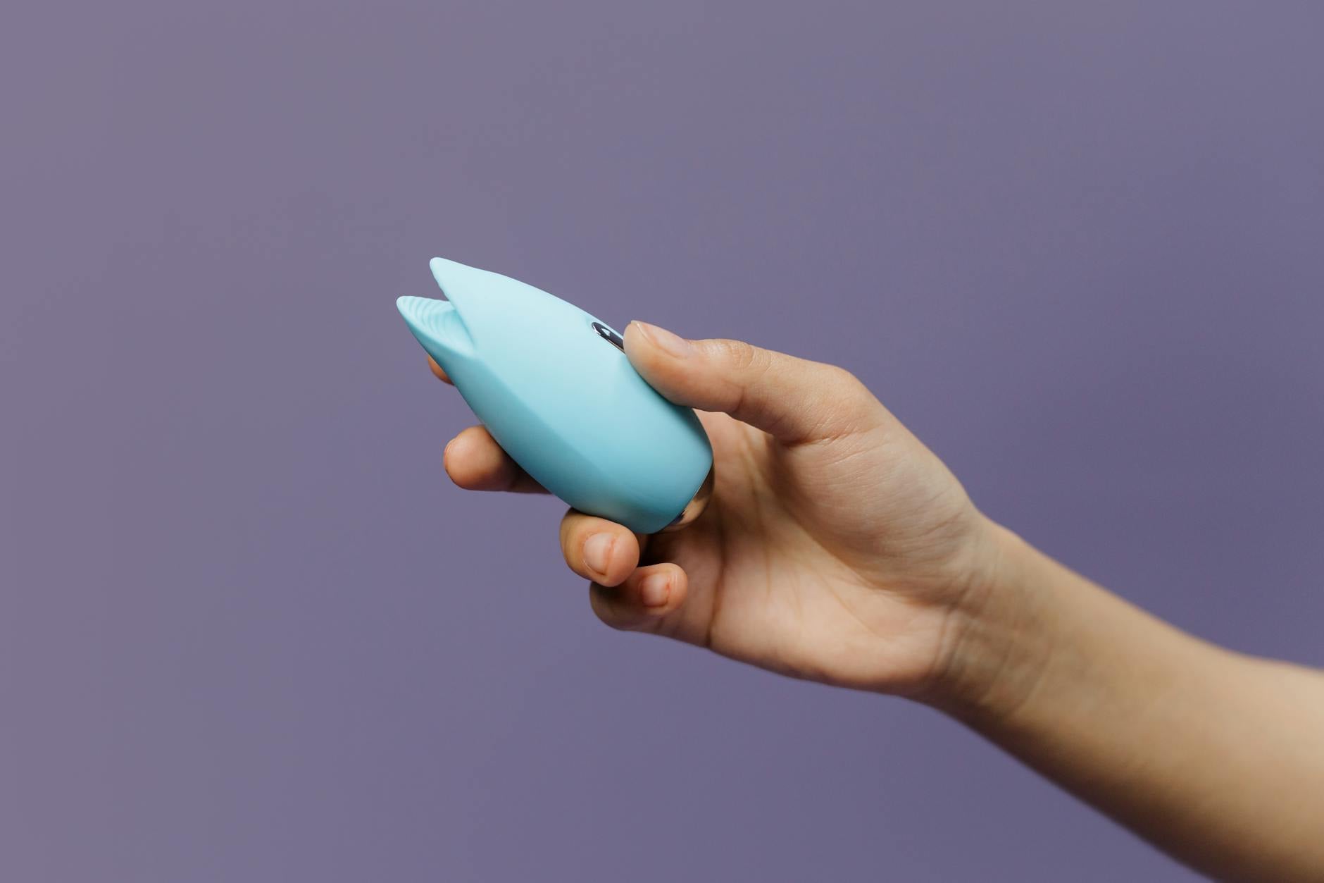 A hand holding a blue silicone sex toy against a purple background, symbolizing pleasure and self-awareness